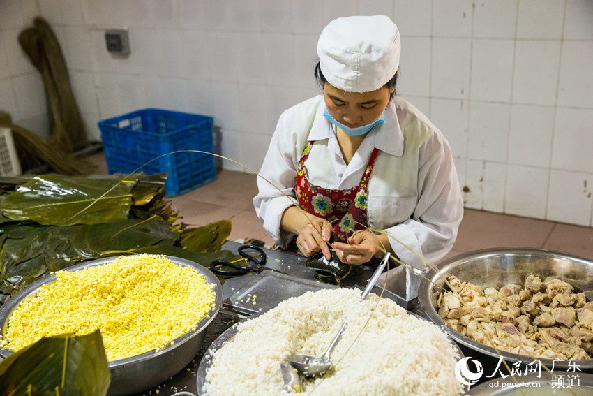 6月17日，广东肇庆市肥仔伟食品有限公司的生产车间内，一名工人正在手工包制肇庆裹蒸粽。传统裹蒸粽是以糯米、去皮绿豆、上等猪肉做原料，用肇庆特产冬叶包裹，延续手工包制的传统，香气横溢，吃后齿颊留香。田伟 摄